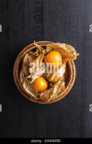 Physalis peruviana in einer Schüssel. Cape Gooseberry oder gemahlene Kirschen Früchte auf schwarzem Tisch. Draufsicht. Stockfoto