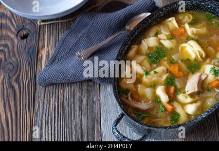 Topf mit frisch gekochter und hausgemachter Hühnersuppe. Gekocht mit Tortellini und serviert auf Holztisch. Overhead-Ansicht mit Kopierbereich Stockfoto