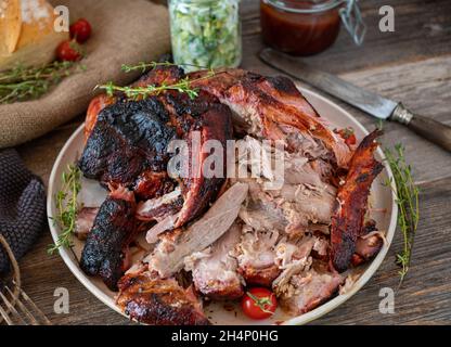 amerikanisches traditionelles Pulled Pork serviert zerfetzt auf einem Teller mit Barbecue-Sauce, Salat und Brot auf einem Holztisch Stockfoto