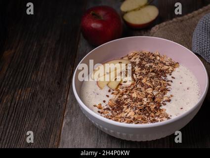 Gesunde Frühstückschale mit frischem Apfeljoghurt, gekrönt mit gerösteten Haferflocken und Leinsamen. Auf Holztisch isoliert serviert Stockfoto