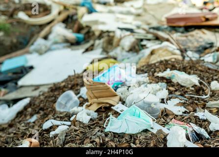 Gebrauchte Gesichtsmaske entsorgen im Hausmüll. Entsorgung von medizinischem Abfall mit unhygienischer Entsorgung. Kontaminierter Abfall in der Gemeinschaft. Einmal-Ohrbügel Stockfoto