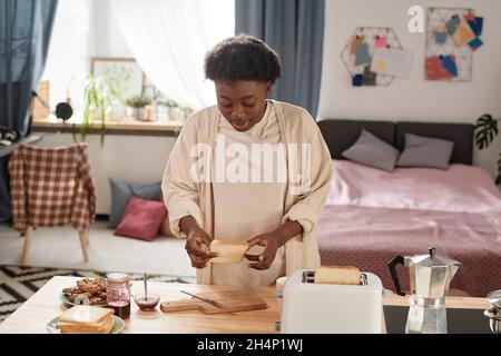 Afrikanische junge Frau, die zum Frühstück in der Küche Toast mit Marmelade macht Stockfoto