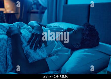 Afrikanische Frau, die in ihrem Bett unter der Decke lag und versuchte, nachts in ihrem Schlafzimmer zu schlafen Stockfoto