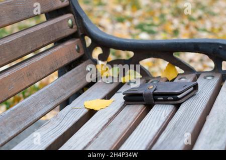 Telefon auf der Bank verloren. Konzept, dass kein Draht abgeklemmt wird. Vergessen oder verloren von jemandem Smartphone auf einer Bank im Park, in einem schäbigen braunen lea Stockfoto