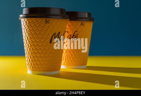 Ukraine, Kiew - 17. Februar 2021: Gelbes Glas Kaffee von McDonald's. Papierglas Getränk McCafe. Kaffeetasse auf Tisch mit Schatten. Speisekarte im Fastfood-Restaurant. Stockfoto