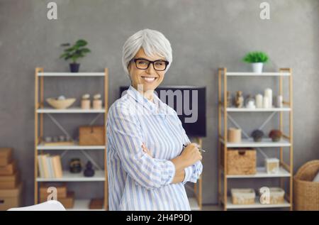 Porträt einer glücklichen älteren Frau, die mit gekreuzten Armen steht und die Kamera anlächelt Stockfoto