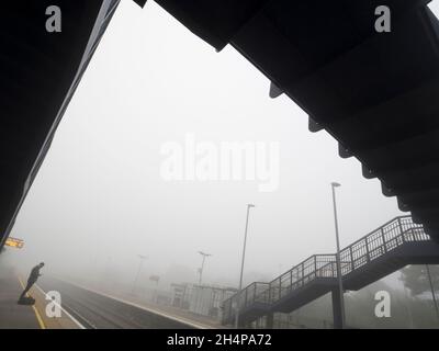 Selbst das alltägliche kann durch Schönheit zur richtigen Zeit und am richtigen Ort verwandelt werden. Hier sehen wir eine einzelne, geduldige Person, die auf den Zug wartet, der eine andere Person einfährt Stockfoto