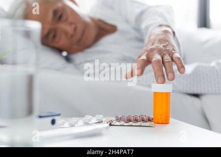 Verschwommener asiatischer Patient, der Pillen in der Nähe von Wasser auf der Krankenhausstation einnahm Stockfoto