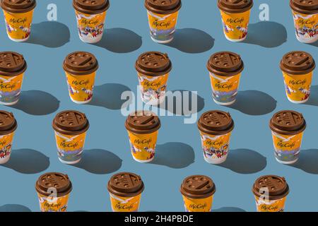 Ukraine, Kiew - 1. November 2021: Musterhintergrund. Gelbes Glas Kaffee von McDonald's. Verschiedene Winter Papier Glas trinken McCafe. Kakaotasse auf dem Tisch mit Schatten. Speisekarte im Fastfood-Restaurant. Stockfoto