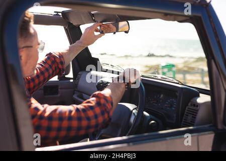 Kaukasischer Mann, der den Rückspiegel im Auto am Meer justiert Stockfoto