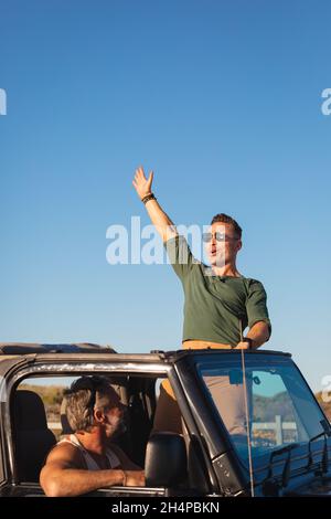 Glücklich kaukasischen Homosexuell männlichen Paar die Arme im Auto am sonnigen Tag am Meer zu heben Stockfoto