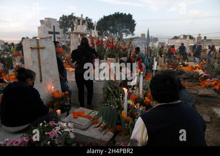 Nicht exklusiv: MEXIKO-STADT, MEXIKO - 2. NOVEMBER 2021: Familienmitglieder schmücken und zünden die Gräber ihrer Lieben an, die im Mixq San Andrés ruhen Stockfoto