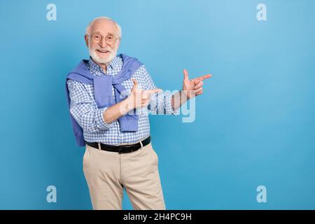 Foto von optimistischen alten grauen Frisur Mann Punkt leeren Raum tragen Brille blaues Hemd isoliert auf pastellfarbenen Hintergrund Stockfoto