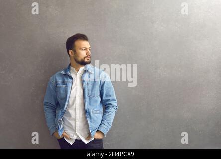 Porträt eines hübschen, ruhigen Mannes in einer Denim-Jacke auf grauem Hintergrund. Stockfoto