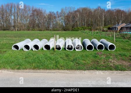 Zehn Betonrohre für das Abwassersystem liegen im Gras einer Wiese Stockfoto