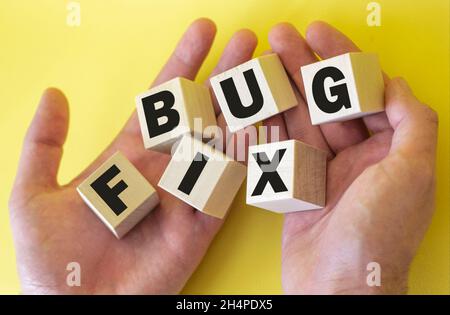 Bugfix, Text wird auf Holzklötze in männlichen Händen auf gelbem Hintergrund geschrieben Stockfoto