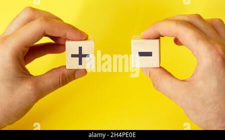 Blöcke in den Händen auf einem gelben Hintergrund mit Plus und Minus Stockfoto