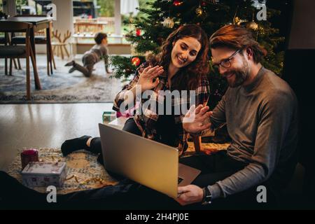 Mann und Frau sitzen zu Hause und führen während der weihnachtszeit einen Videoanruf auf dem Laptop. Ein Paar begrüßt Freunde während eines Videoanrufs. Stockfoto