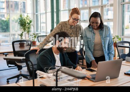 Lächelnde Gruppe verschiedener Geschäftsleute, die an einem Laptop arbeiten Stockfoto
