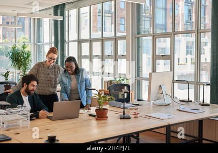 Lachende Gruppe verschiedener Geschäftsleute, die an einem Laptop arbeiten Stockfoto