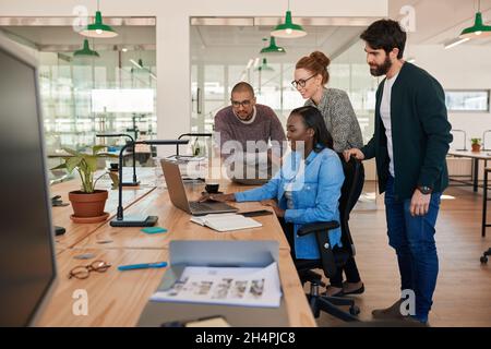 Lächelnde Gruppe verschiedener Geschäftsleute, die zusammen an einem Laptop arbeiten Stockfoto