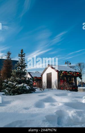 Gemütliche kleine Vintage-Holzhäuser mit Neujahrsspielzeug und Girlanden. Straßenszene mit Schnee und blauem bewölktem Himmel. Neujahr und Weihnachten bei Stockfoto