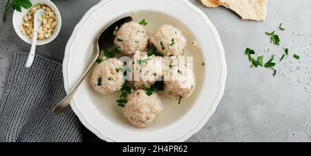 Hausgemachte Hähnchenmatzokugelsuppe mit Petersilie und Knoblauch in einfacher weißer Keramikplatte auf grauem Stein oder Beton. Traditioneller jüdischer Pass Stockfoto