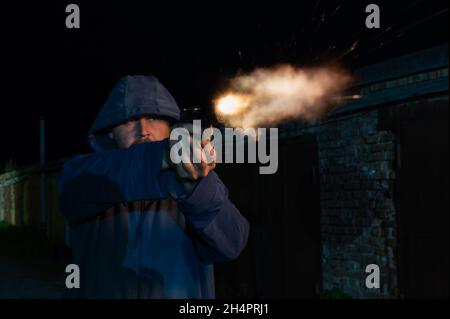 Kaukasischer Mann in einer Kapuze schießt eine Pistole. Stockfoto