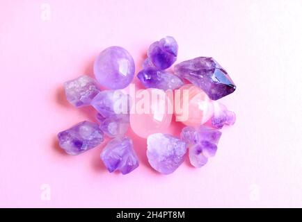 Mineralien von Edelsteinen auf rosa Hintergrund. Wunderschöne violette Amethyst-Kristalle und Rosenquarz-Mineralien Stockfoto