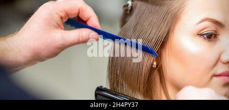 Friseur glättet weibliche braune Haare von mittlerer Länge mit einem Haar mit einem Eisen Haarglätter und Kamm in einem Schönheitssalon Stockfoto