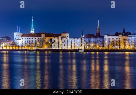 Nachtansicht des historischen Stadtzentrums mit Schloss und Kirchen vom Ufer des Daugava Flusses mit Straßenlaternen, Riga, Lettland Stockfoto