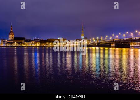 Nachtansicht des historischen Stadtzentrums und der Steinbrücke vom Ufer des Daugava Flusses mit Straßenlaternen, Riga, Lettland Stockfoto