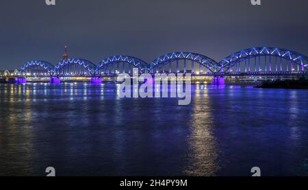 Nachtansicht der Eisenbahnbrücke vom Ufer des Daugava Flusses mit Straßenlaternen, Riga, Lettland Stockfoto