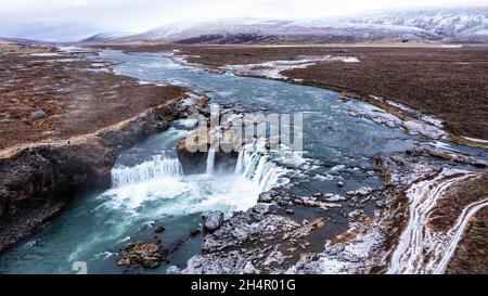 Drohnenaufnahme des Hufeisenwasserfalls Godafoss, Island, aus einem hohen Winkel aufgenommen. Luftaufnahme der mächtigen Kaskade, des Flusses und der schneebedeckten Felsen. L Stockfoto