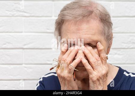 Nahaufnahme einer ungesunden älteren Frau, die eine Brille auszieht, massiert die Augen, die an starker Migräne oder Kopfschmerzen leiden, krank, ältere Großmutter st Stockfoto