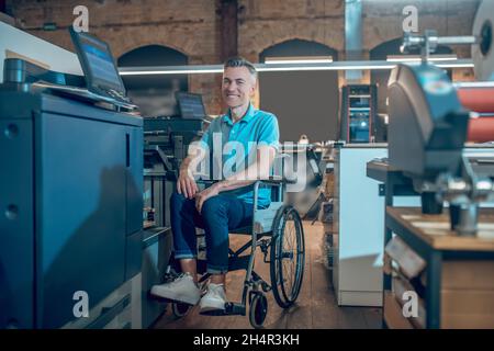 Lächelnder Mann im Rollstuhl in der Nähe von Bürogeräten Stockfoto