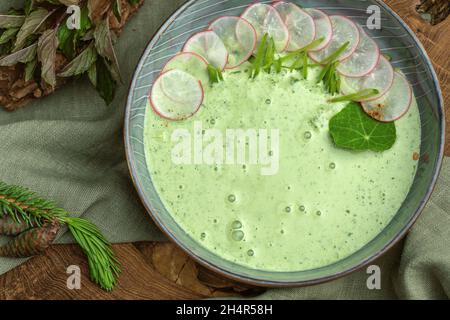 Erfrischende kalte grüne Gurke, Avocado, Radish, Joghurt und Minzsuppe in einer Schüssel auf Holzhintergrund. Vegetarisches Speisekonzept Stockfoto