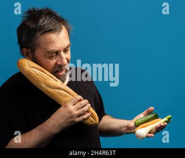 Gesundes Lifestyle-Konzept. Harte Wahl. Was ist besser Brot oder Gemüse. Ein Mann mittleren Alters in einem schwarzen T-Shirt hält Apfel in einer Hand und Brot in der Hand Stockfoto