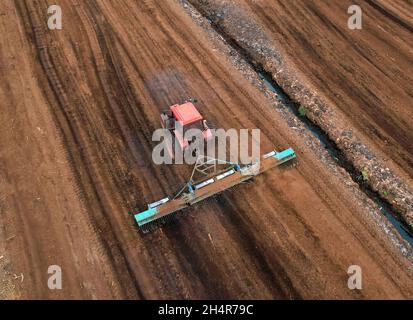 Torf-Harvester-Traktor zum Sammeln von entpackenden Torfböden. Bergbau und Ernte von Torfland. Die aus dem Schlamm entwässerten Flächen werden für die Torfgewinnung verwendet. Abfluss Stockfoto