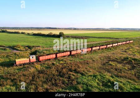 Train transportiert Torf in Güterwagen aus der Torfgewinnung. Luftaufnahme der Diesellokomotive auf der Eisenbahn in der Landschaft an Feuchtgebieten. Drohnenansicht von Stockfoto