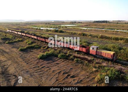 Train transportiert Torf in Güterwagen aus der Torfgewinnung. Luftaufnahme der Diesellokomotive auf der Eisenbahn in der Landschaft an Feuchtgebieten. Drohnenansicht von Stockfoto