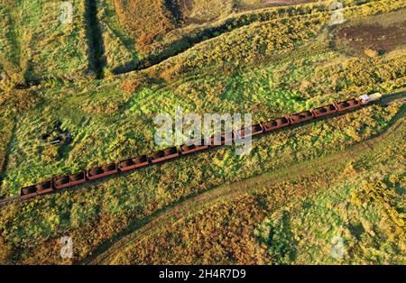 Train transportiert Torf in Güterwagen aus der Torfgewinnung. Luftaufnahme der Diesellokomotive auf der Eisenbahn in der Landschaft an Feuchtgebieten. Drohnenansicht von Stockfoto