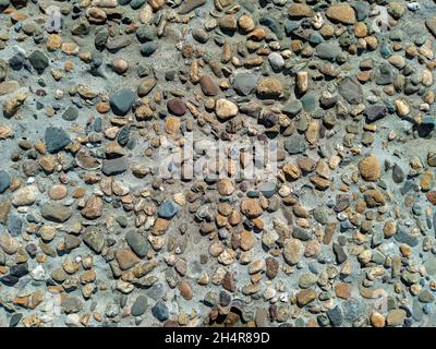 Betonoberfläche von Groyne mit farbigen Kiessteinen aus dem Meer in verschiedenen Formen, Hintergrund Stockfoto