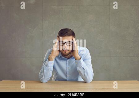 Unglücklicher junger Mann, der unter starken Kopfschmerzen leidet und den Finger gegen die Schläfe drückt Stockfoto
