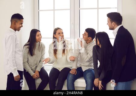 Gruppe von glücklichen jungen, multirassischen Mitarbeitern oder Freunden, die über lustige Sachen reden und lächeln Stockfoto