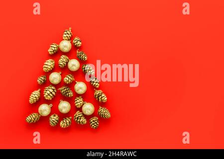 Neujahrskarte. Abstrakter Weihnachtsbaum aus goldenen Zapfen mit Verzierungen auf rotem Hintergrund. Minimales Weihnachtskonzept. Draufsicht, Kopierbereich Stockfoto