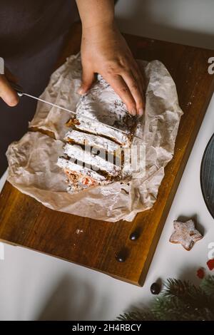 Baker schneidet weihnachtliche Backwaren, Stollen auf einem Holzbrett Stockfoto