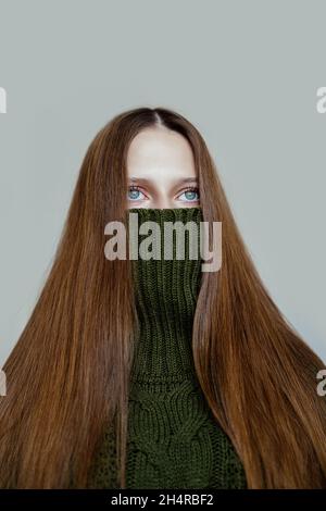 Modernes Porträt eines Mädchens in einem grünen Pullover, das ihr Gesicht wie in einer Schutzmaske versteckt Stockfoto