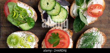 Banner mit verschiedenen Gemüse-Sandwiches mit Frischkäse, Tomaten, Dill, Gurken, Lauch und Basilikum. Serviert ein vegetarisches Sandwiches für Vorspeisen auf Schneidebrett. Draufsicht flach legen Stockfoto