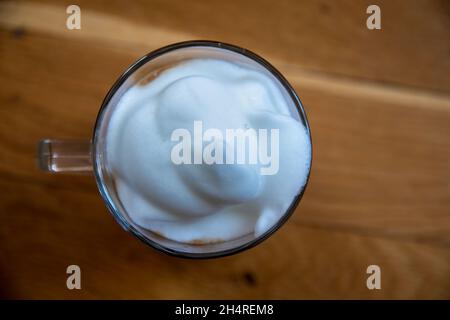 Eine Tasse Kaffee aus Glas mit weißem Milchschaum auf einer Holzoberfläche Stockfoto